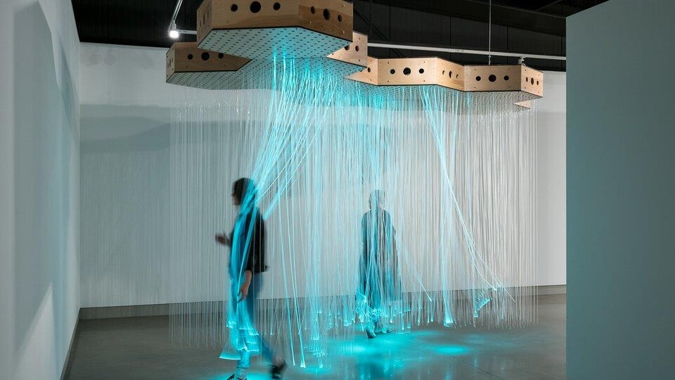 Deux badauds déambulent parmi des fibres optiques turquoises dans un musée d'art contemporain.
