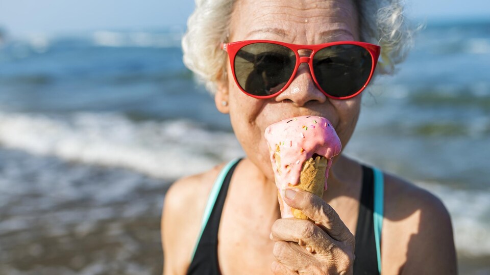 Une femme d'âge mûr mange une crème glacée sur le bord de la plage.