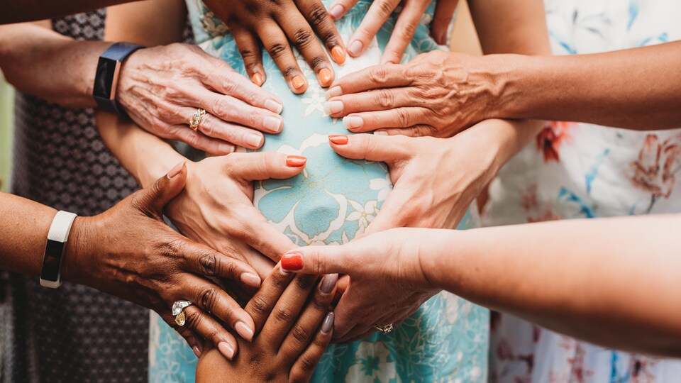 Plusieurs mains touchent le ventre d'une femme enceinte.