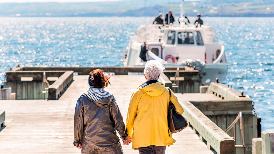 Deux personnes marchent sur un quai, en direction d'un petit bateau.