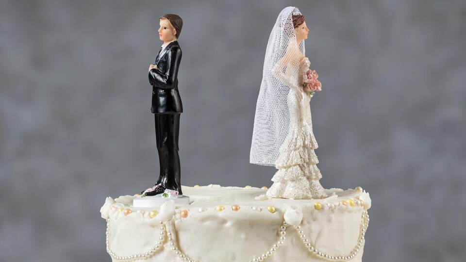 Photo de deux figurines de mariés qui se tournent le dos sur le dessus d'un gâteau de mariage.