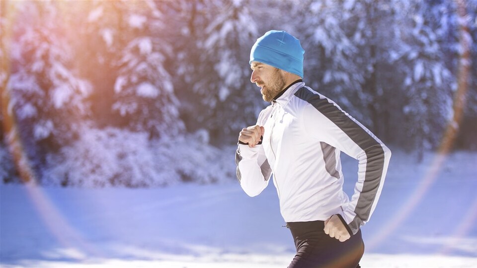 Un homme pratique la course sur un sentier et devant des arbres enneigés.