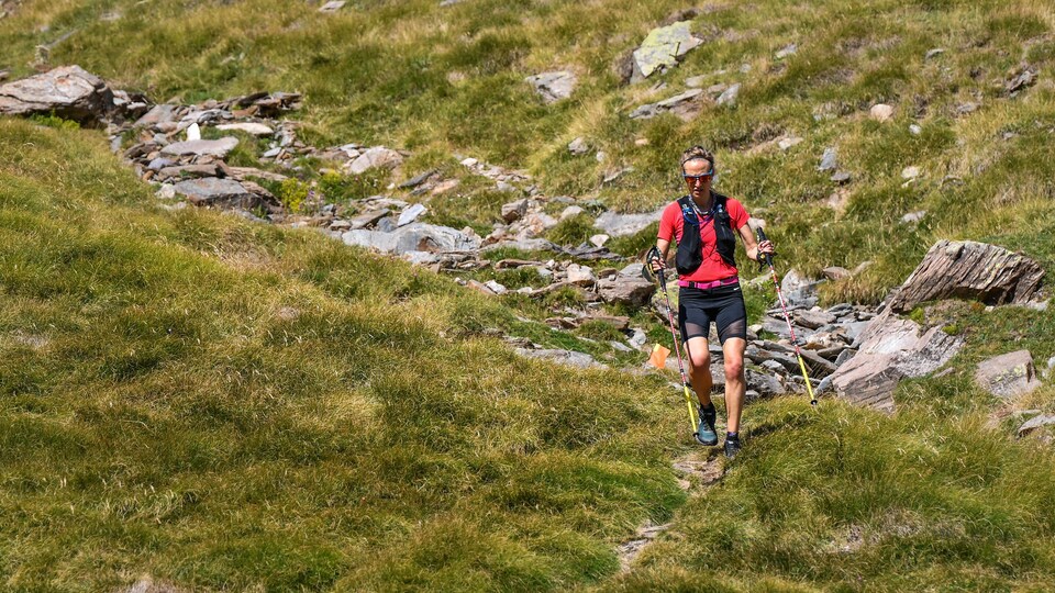 Une femme court dans des sentiers de montagne, des bâtons de marche à la main.