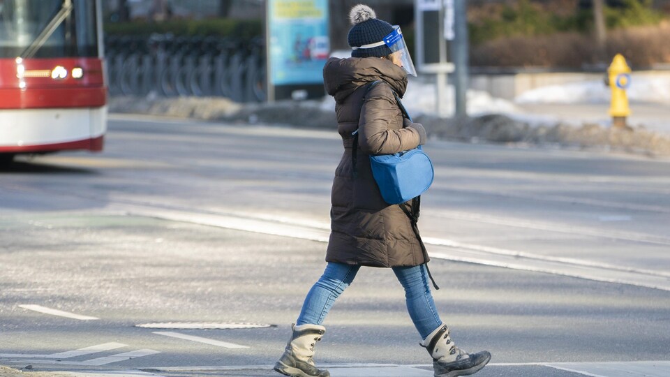 Une personne portant des vêtements d'hiver et une visière traverse la rue devant le tramway.