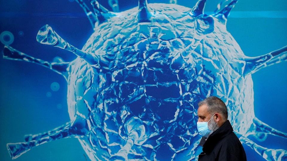 Un homme porte un masque devant une illustration géante de la molécule du SRAS-CoV-2.