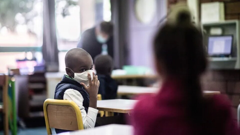 Un élève portant un masque se retourne vers un autre élève dans une salle de classe.