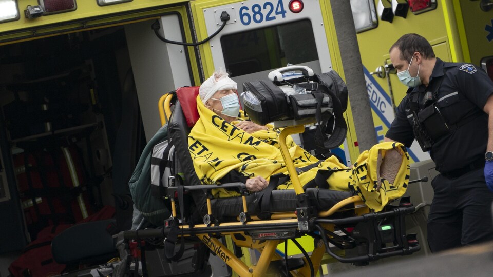 Un ambulancier s'occupe d'un patient allongé sur une civière près d'une ambulance dont la porte arrière est ouverte.
