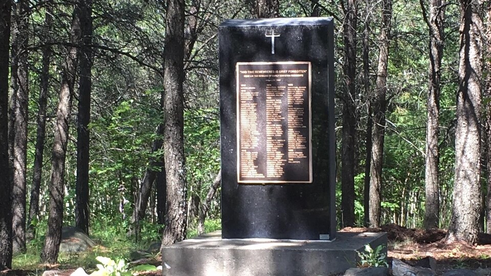 Une grande pierre porte une croix et une plaque avec une grande liste de noms des personnes enterrés sur l'ancien site funéraire de Coniston.