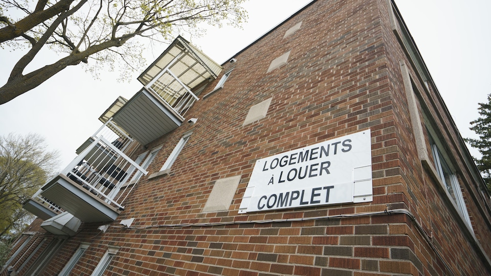 Une affiche accrochée à un immeuble sur laquelle est écrit : logement à louer, complet.