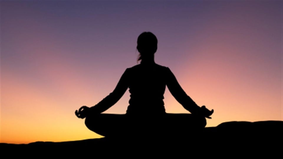 Silhouette d'une personne assise en position de méditation au coucher du soleil.