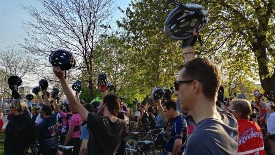 Des cyclistes réunis au parc du Pélican, à Montréal, lèvent leur casque de vélo dans un moment de silence.