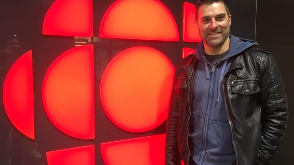 Daniel LeBlanc, debout devant le logo illuminé de Radio-Canada.