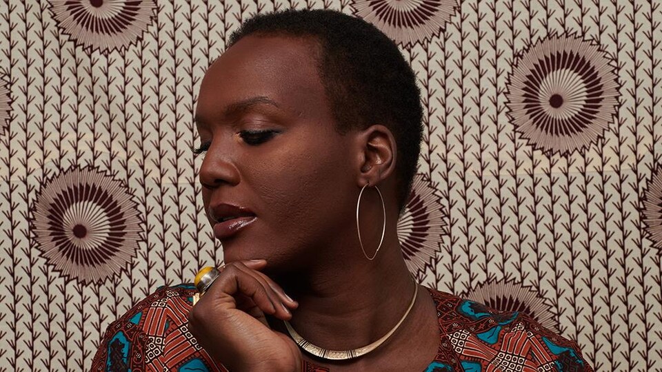 Alicia, de profil. les yeux baissés, devant un fond aux motifs africains.