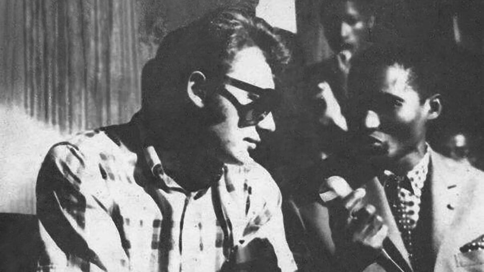 Marcel Bilé a un micro à la main, Johnny Hallyday le regarde, il porte des lunettes de soleil.
