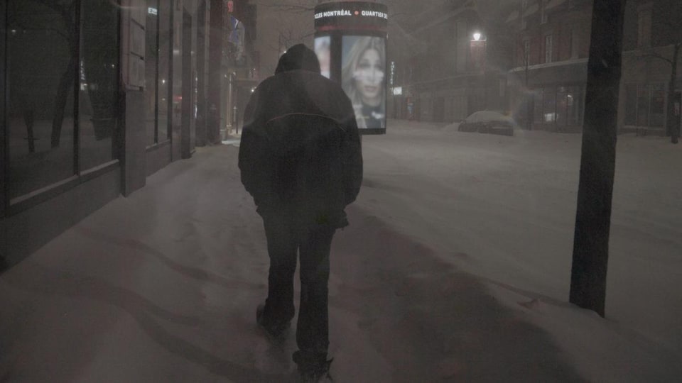 Un itinérant, de dos, marche dans la neige.