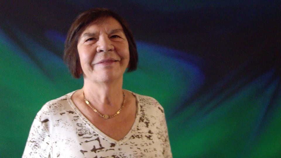 Rita Letendre pose devant un fond vert et bleu.