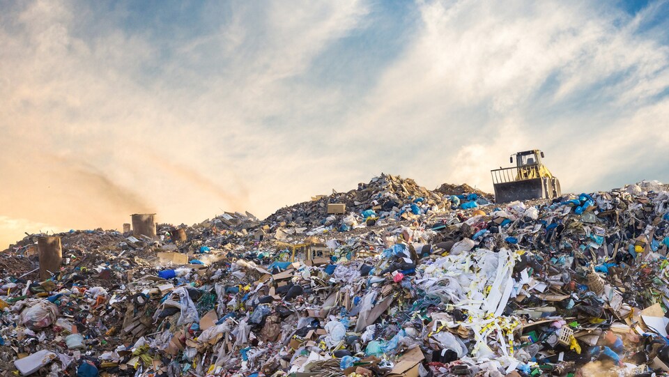 Un véhicule repousse des piles de déchets dans un dépotoir.