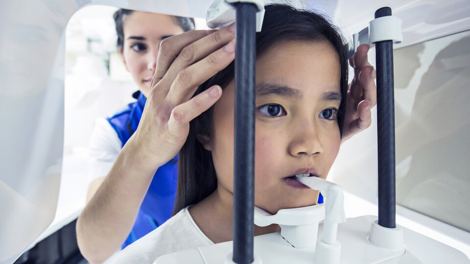 Une infirmière ajuste le visage d'une fille sur une machine de radiographies dentaires.