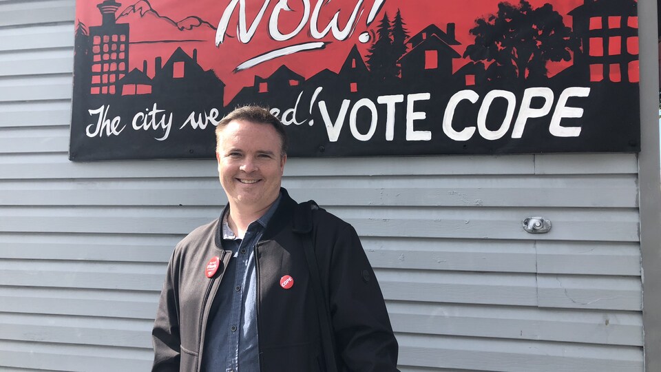 aspirant politicien souriant devant un mur placardé
