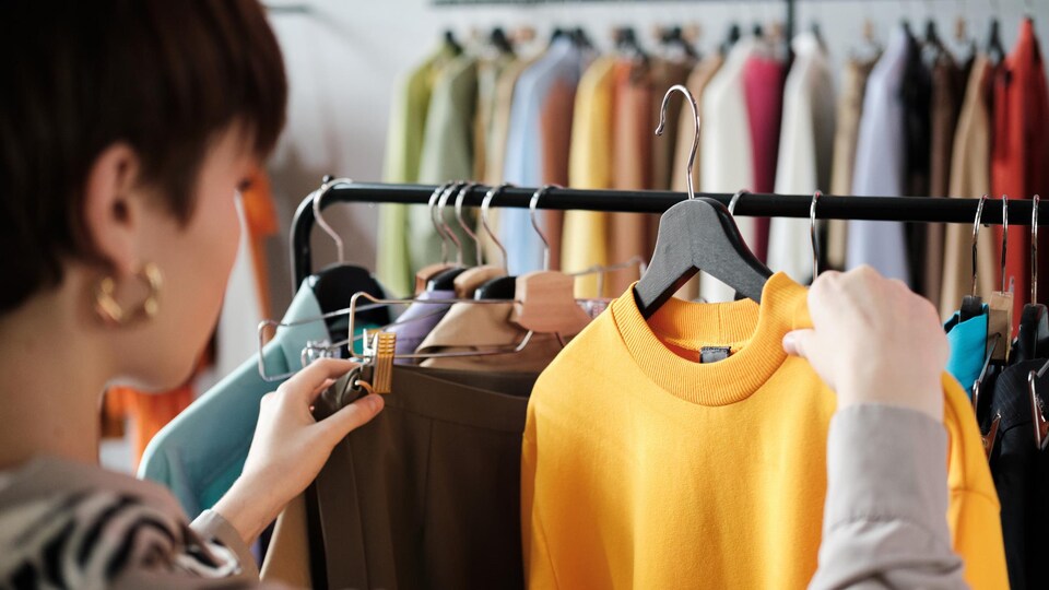 Vue arrière d'une femme regardant des vêtements sur des cintres accrochés à un présentoir dans un magasin.