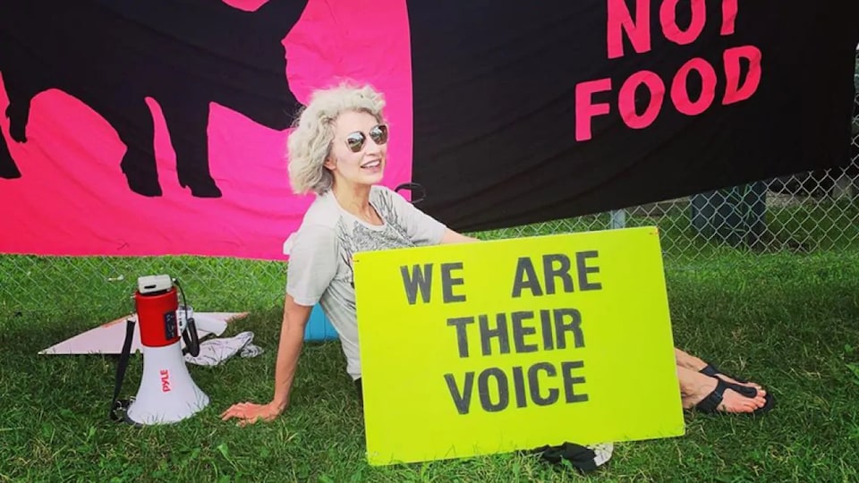 Une femme tenant une affiche disant «nous sommes leur voix» assise dans la pelouse.