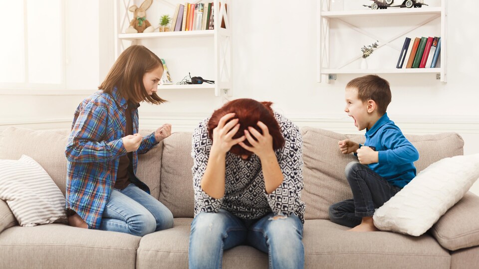 Une mère à l'allure excédée se prend la tête pendant que ses enfants se disputent.