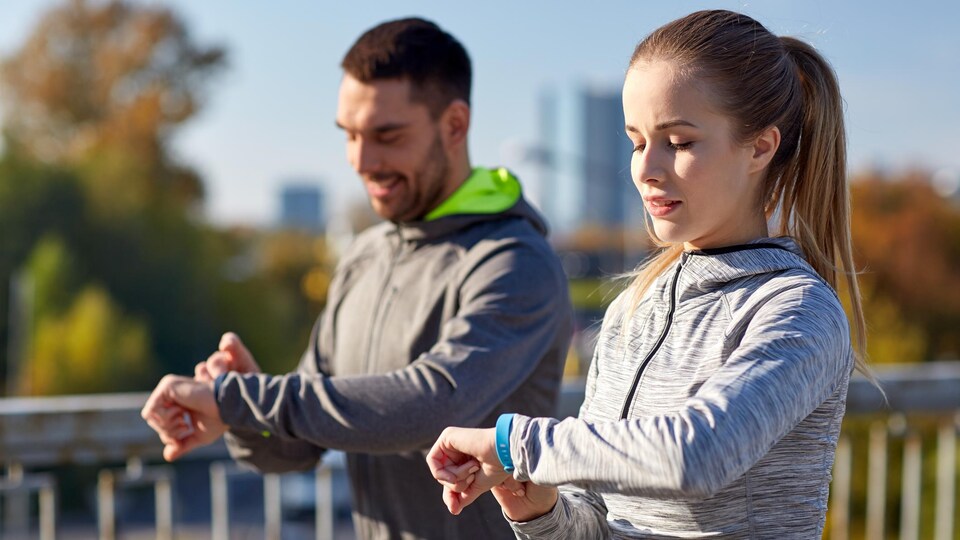 Deux sportifs à l'extérieur consultent leur bracelet connecté.