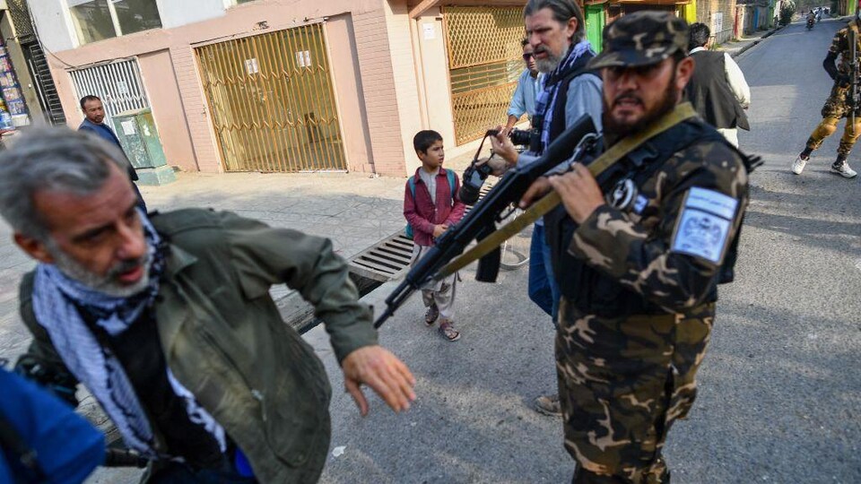 Un membre des forces spéciales talibanes pousse un journaliste avec son fusil.