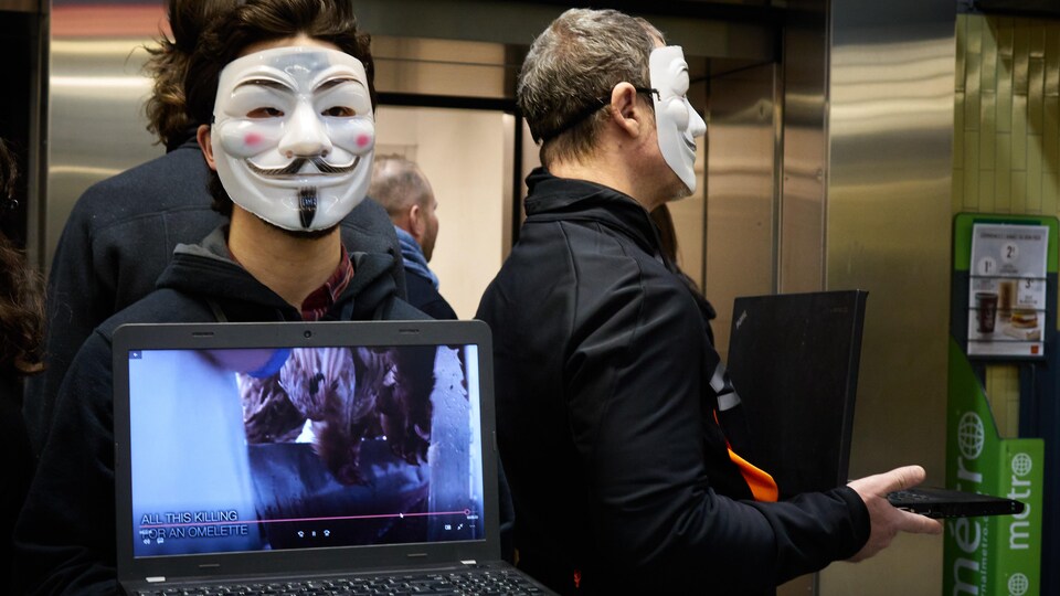 Des personnes portant un masque de Anonymus tenant un ordinateur portable dans lequel on y voit des image de carnage d'animaux                       