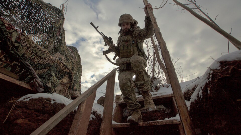 Un homme armé en habit de combat descend dans une tranchée.