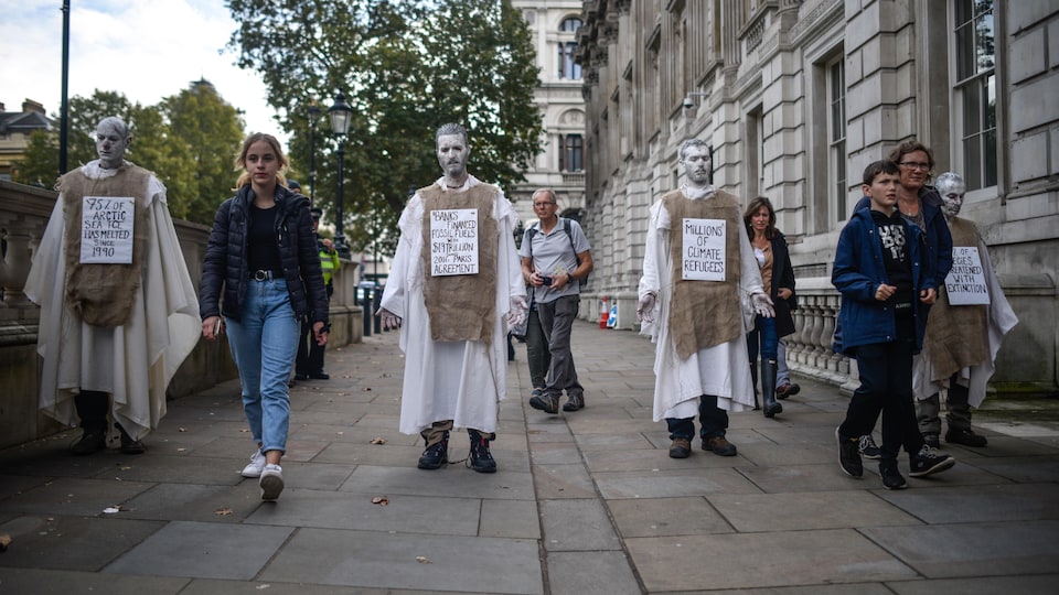 Des personnes maquillés de blanc déambulent vêtus de toges et de pancarte sur le climat. 