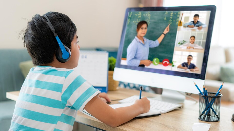 Un garçon devant un ordinateur assiste au cours donné par son enseignante.