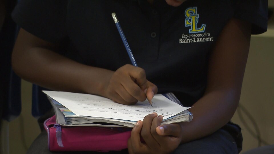 Un élève vêtu d'un polo de l'école secondaire Saint-Laurent écrit dans son cahier.