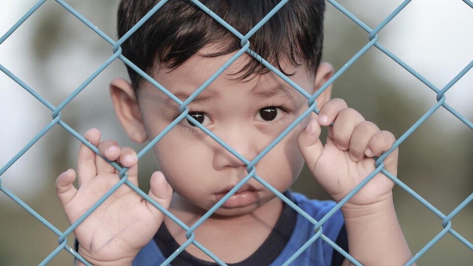 Un enfant derrière une clôture de métal.