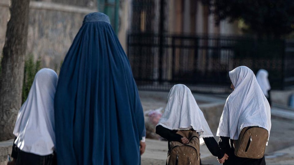 Une femme afghane marche avec de jeunes écolières.