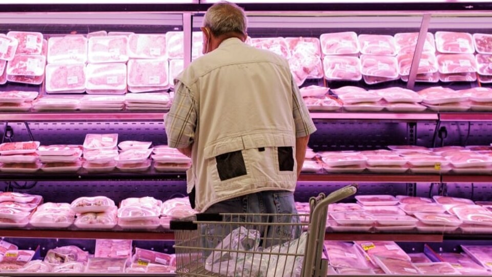 Un homme devant le rayon viandes d'un supermarché.