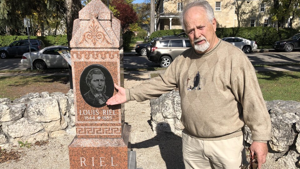 Un homme montre un monument avec une image de Louis Riel.