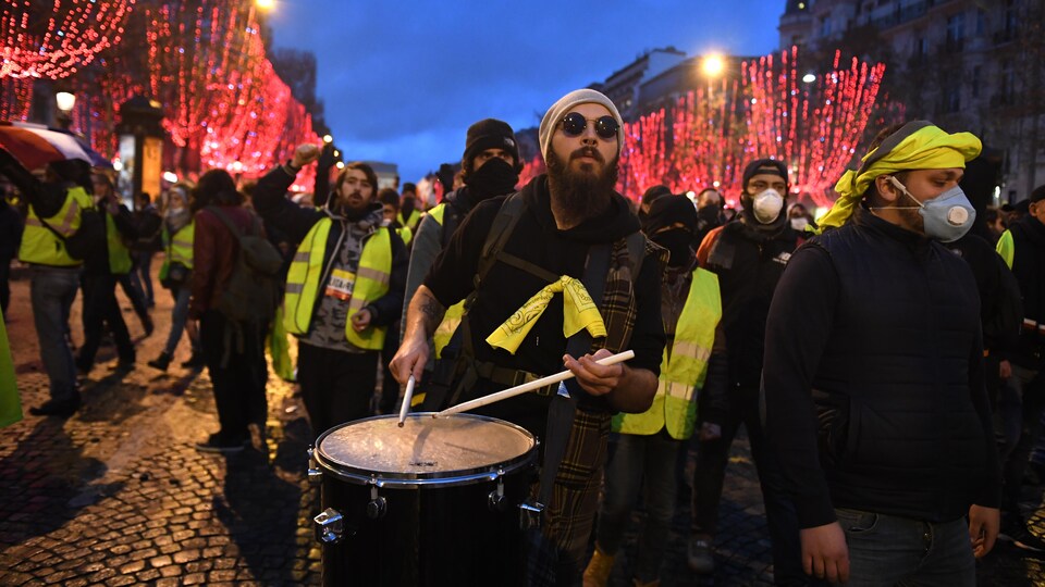 Des manifestants marchent sur les Champs-Élysées en battant le tambour.