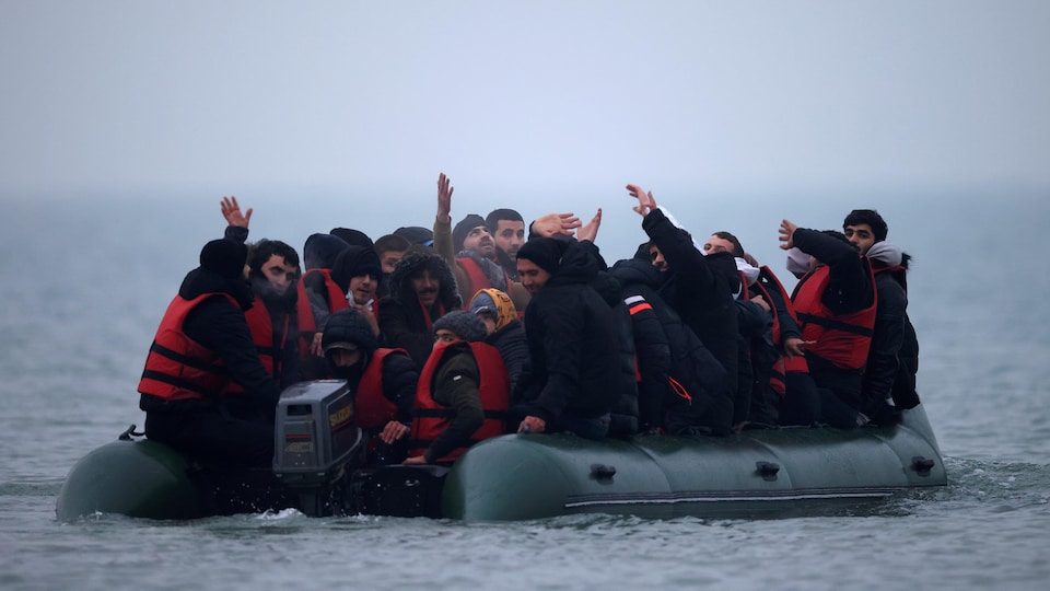 Des hommes entassés sur un bateau gonflable lèvent les bras dans les airs.