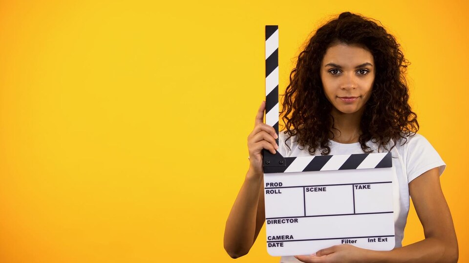 Une femme à la peau noire tient un clap de cinéma dans ses mains.