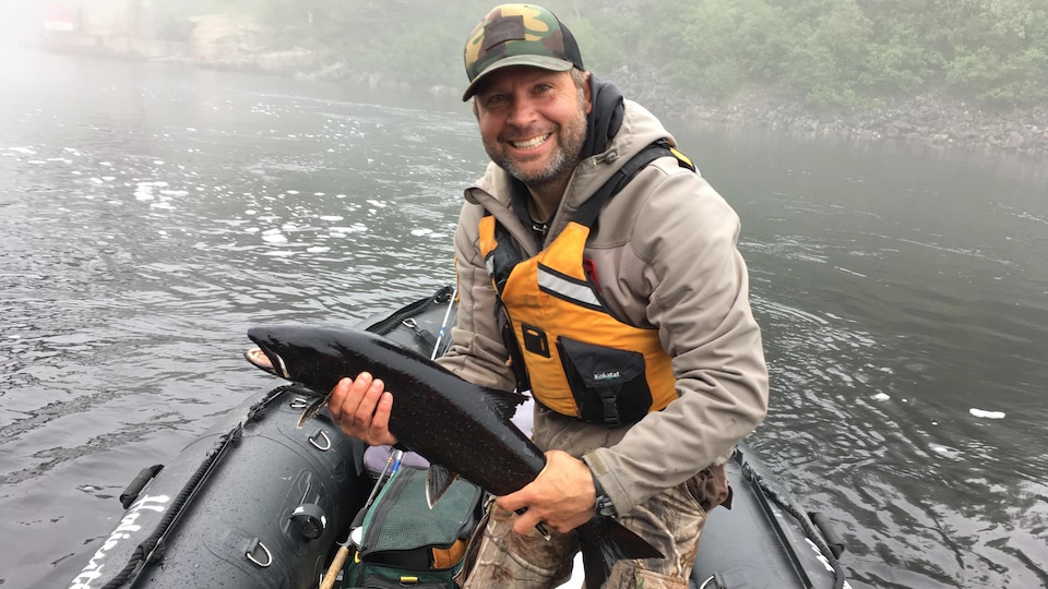 Dominick Cuerrier, pêcheur, dans un bateau sur l'eau, avec un poisson dans les mains.