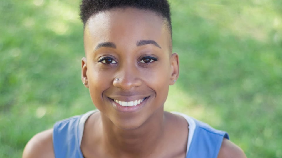 Une personne à la peau noire et aux cheveux courts sourit dans un parc.