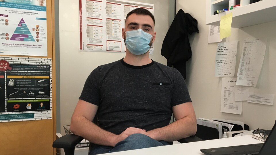Un homme portant un masque médical, assis derrière un bureau.
