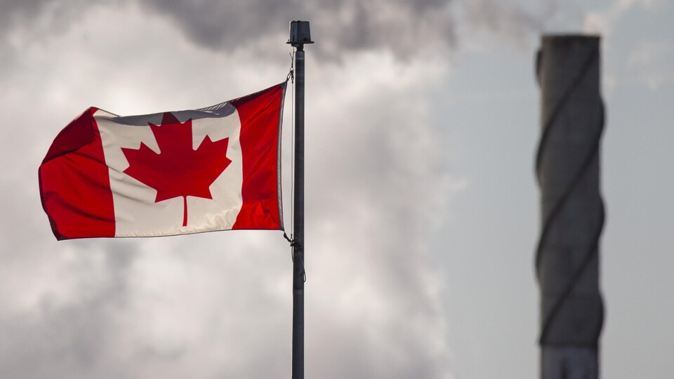 Un drapeau canadien avec, en arrière-plan, de la fumée qui sort d'une cheminée.