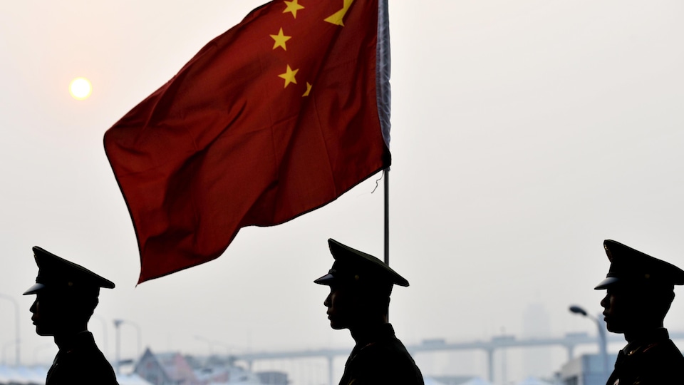 Des soldats chinois passent à côté d'un drapeau de la Chine, à Shanghai.