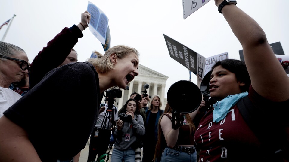 Deux groupes de femmes s'opposent, pancartes en main, et scandent des slogans devant les médias rassemblés en face du bâtiment de la Cour suprême. 