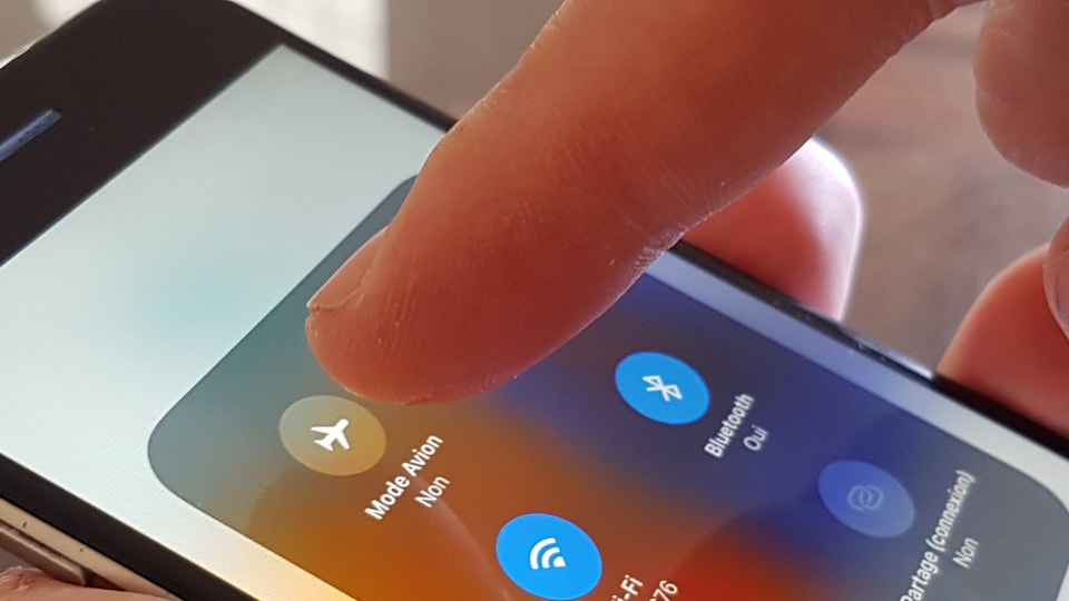 Gros plan sur un doigt qui va appuyer sur l'icone mode avion d'un téléphone intelligent.