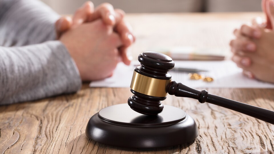 Le marteau de la justice est devant les mains d'un couple sur une table en bois.