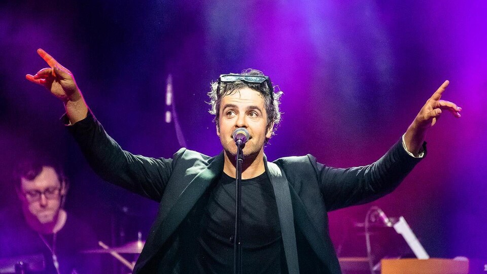 Sur une scène, le chanteur Dumas a les deux bras levés.