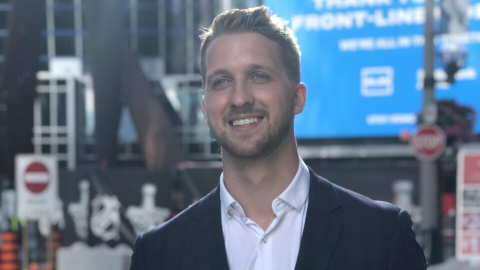 Un homme portant chemise et veston, souriant pour les caméras